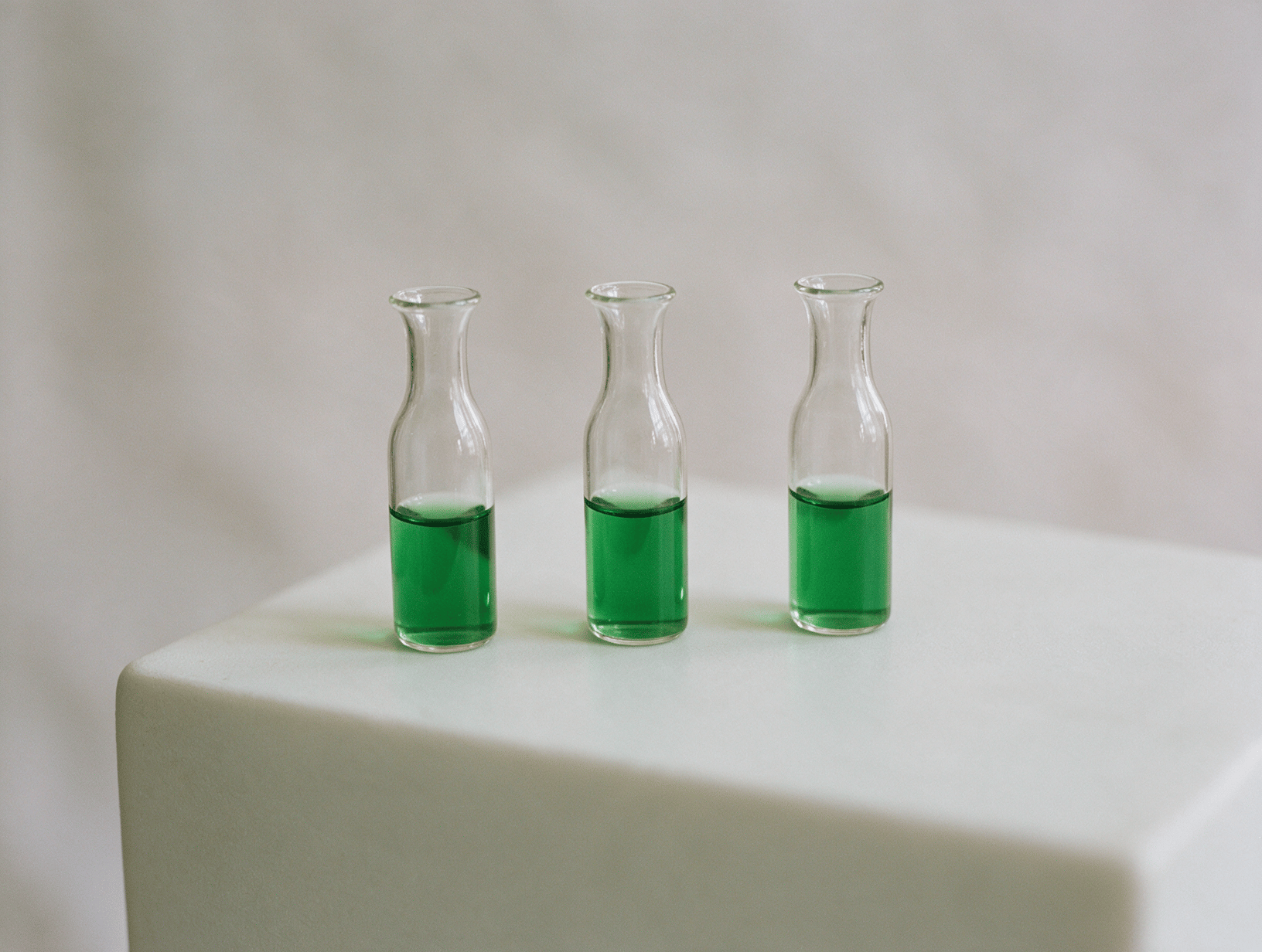 Three small glass vials in a row on a pale plinth