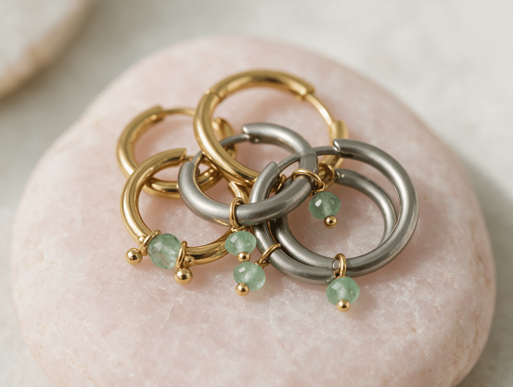 Gold and titanium hoop earrings on pale pink stone