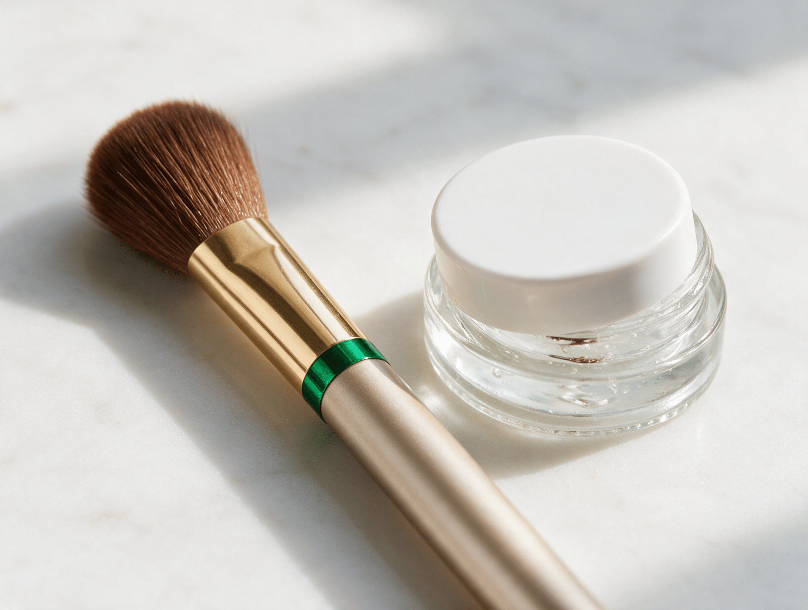 A soft brow brush and a small jar of clear brow gel on white marble
