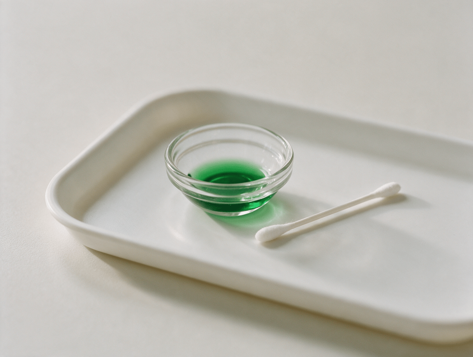 A small glass dish and a cotton swab on a white tray