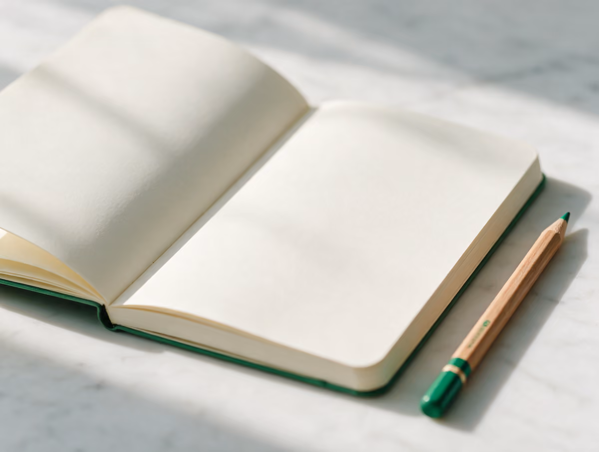 An open blank notebook with a pencil on white marble